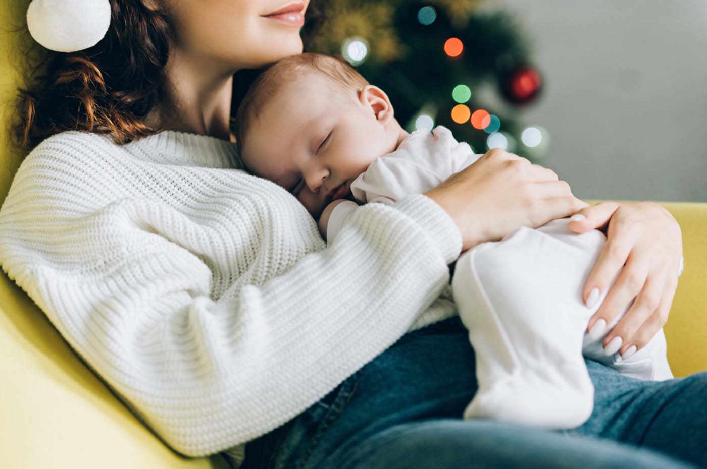 Young white mom with sleeping baby in front of Christmas tree