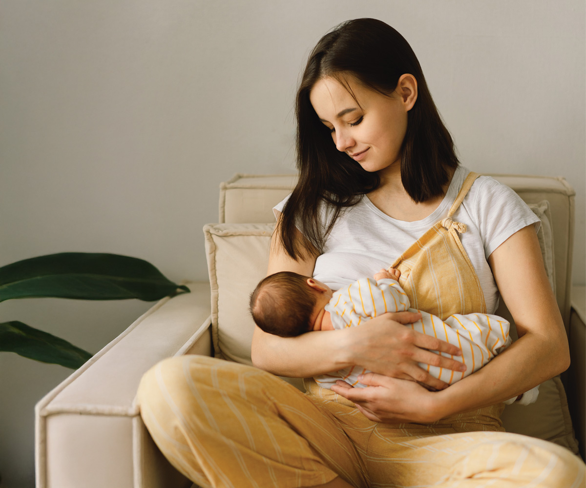 Young mother in a comfortable chair breastfeeding her baby