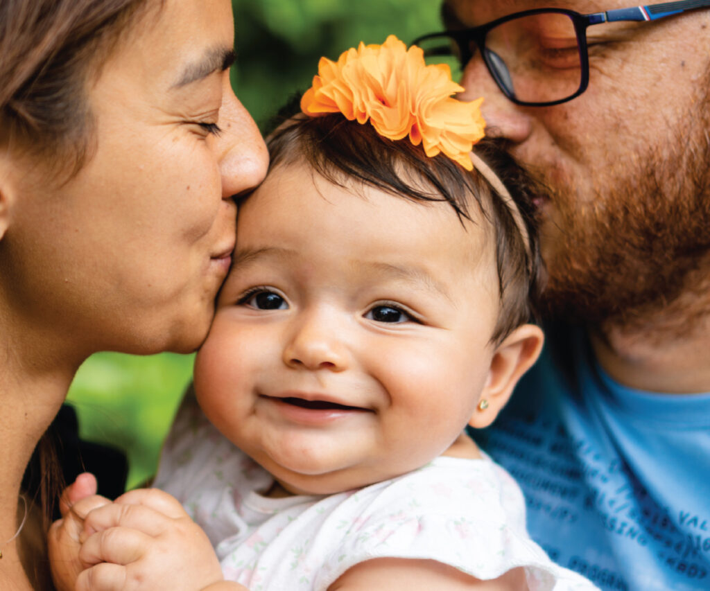 Young mom and dad kissing their smiling baby girl