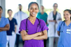Smiling nurse in purple scrubs standing in front of a group of nurses and doctors leading them